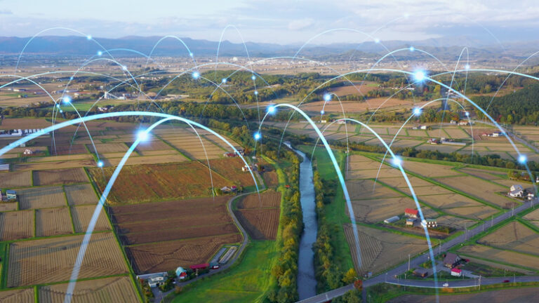 Aerial view of a rural landscape with a river running through it, dotted with farms, fields in various states of harvest, and roads. Overlaid are numerous arcs with nodes, symbolizing a network of wireless connections linking the area.